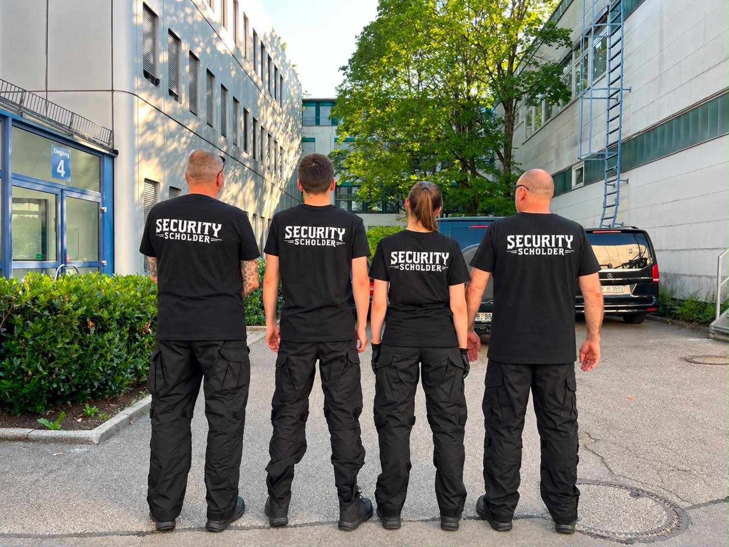 Dieselben vier Sicherheitskräfte von hinten, Aufdruck Security Scholder auf den T-Shirts